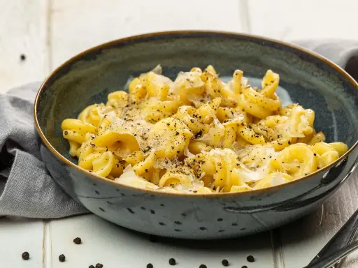 Eine Schüssel mit italienischen Nudeln, bestreut mit Parmesan und schwarzem Pfeffer, serviert auf einem rustikalen Tisch.
