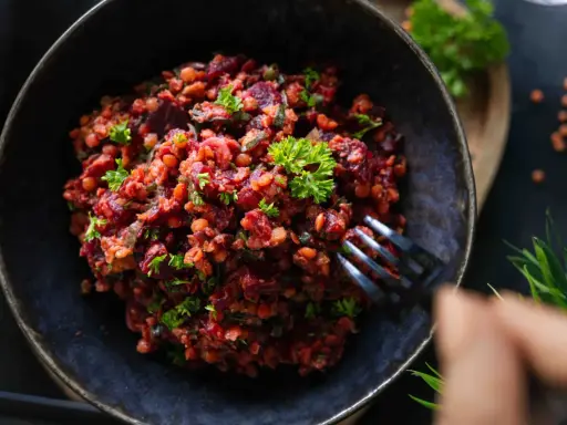 Ein köstlicher rote Linsen Salat mit Roter Bete und frischer Petersilie, serviert in einer dunklen Schüssel.