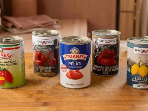 Fünf Dosen mit verschiedenen Tomatenprodukten für Pizza, darunter ganze, geschälte und Datterini-Tomaten.