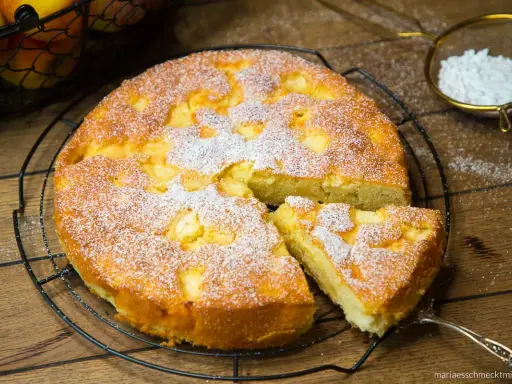 Ein saftiger, versunkener Apfelkuchen nach Omas Rezept, bestäubt mit Puderzucker. Ein Stück wurde bereits herausgenommen.