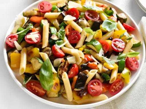Bunter Nudelsalat ohne Mayo mit Penne, gegrilltem Gemüse wie Zucchini, Aubergine, Paprika und Kirschtomaten, garniert mit Basilikum und Parmesan.