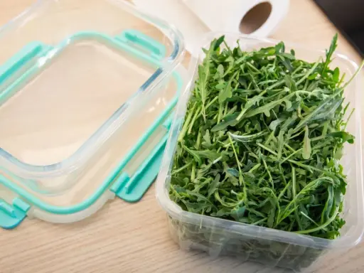 Frischer Rucola Salat in einer Plastikschale, bereit für die Aufbewahrung in einem Glasbehälter.