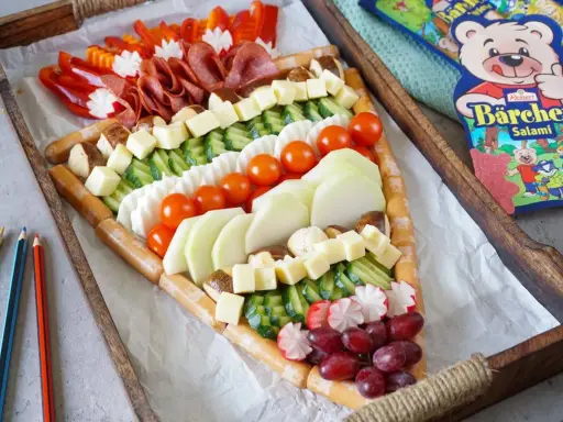 Bunter Fingerfood-Käse-Wurst-Teller in Pizzastückform, perfekt für die Einschulung. Mit Würstchen, Käse, Gurken, Tomaten, Radieschen, Trauben und Salami.
