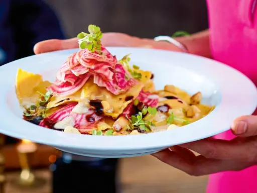 Ein Teller mit Ravioli, garniert mit Streifen von roter Bete und Kräutern. Ein Gericht, das perfekt für "Das perfekte Dinner Rezepte" wäre.