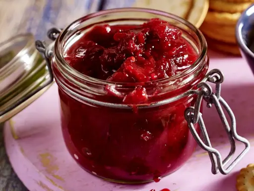 Ein Glas mit leuchtend rotem Zwetschgen-Chutney, bereit, zu Käse oder Gebäck serviert zu werden.