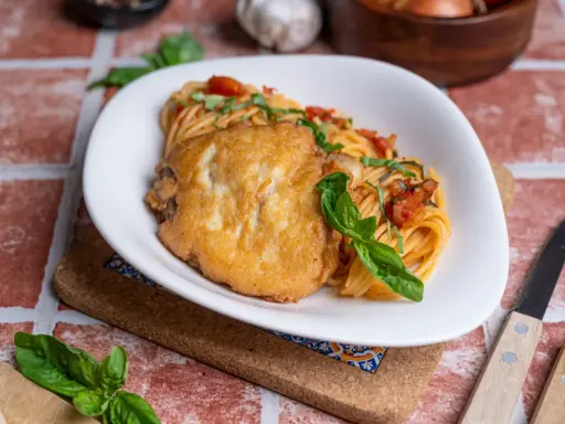 Ein Teller Spaghetti mit Tomatensauce und einem panierten Schnitzel, das ist Piccata. Frisch garniert mit Basilikum.