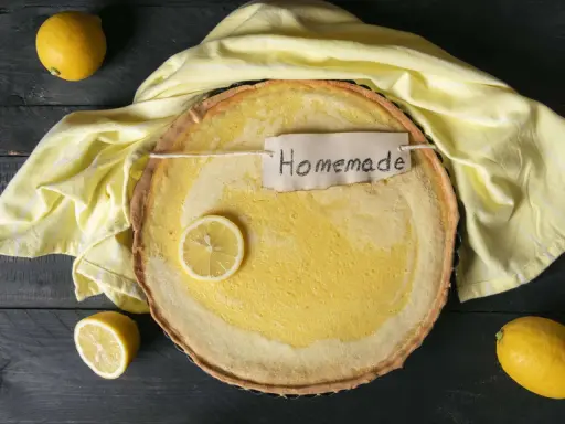 Ein frisch gebackener Joghurt Zitronen Kuchen mit einer Zitronenscheibe und dem Schriftzug "Homemade" auf einem gelben Tuch.