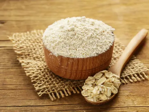 Holzschale mit feinem Hafermehl und Löffel voller Haferflocken. Perfekt zum Backen mit Hafermehl.