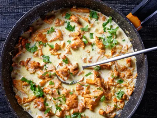 Pfifferlinge in cremiger Rahmsauce, garniert mit Petersilie, in einer Pfanne. Ein Löffel ragt aus der köstlichen Speise.