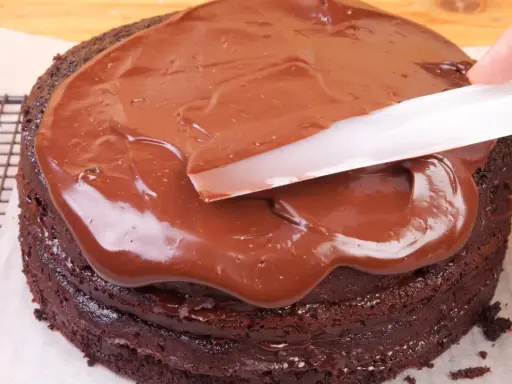 Schokoladenkuchen wird mit glatter, glänzender Ganache überzogen. Was ist eine Ganache? Eine köstliche Mischung aus Schokolade und Sahne.