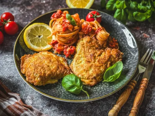 Piccata Milanese mit Pasta und frischen Tomaten, garniert mit Basilikum und Zitrone. Ein köstliches Gericht, das Appetit macht.