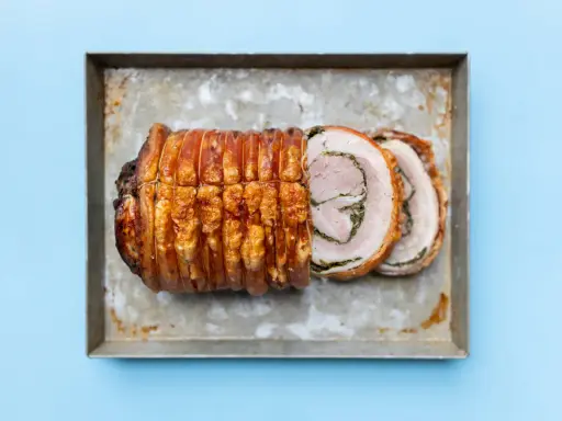 Ein knusprig gebratenes Stück Porchetta, ein italienisches Schweinebraten-Gericht, liegt auf einem Blech.