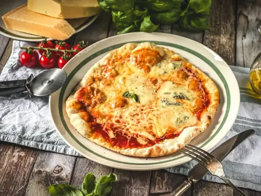 Eine köstliche Pizza Quattro Formaggi mit vier Käsesorten, serviert mit frischen Tomaten und Basilikum auf einem Holztisch.