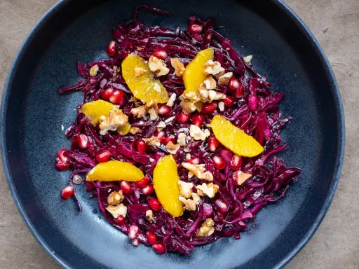 Ein bunter rotkohl salat mit Orangenfilets, Granatapfelkernen und Walnüssen in einer dunklen Schüssel.