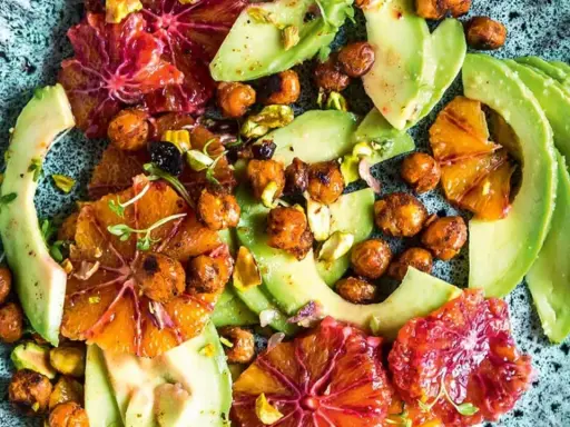 Ein bunter Avocado-Salat mit Blutorangen, Kichererbsen und Pistazien auf einem rustikalen Teller.