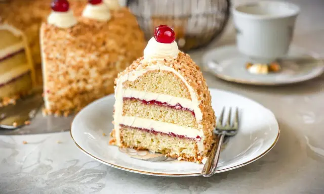 Ein Stück Frankfurter Kranz mit Buttercreme und Kirschen, umhüllt von gehackten Nüssen. Ein Genuss für jeden Kaffeetisch.