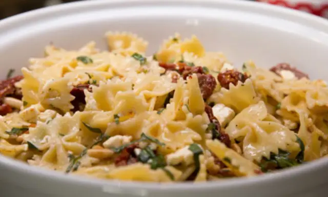 Farfalle-Nudelsalat mit getrockneten Tomaten, Feta und Pinienkernen, garniert mit frischen Kräutern. Ein köstliches Gericht.