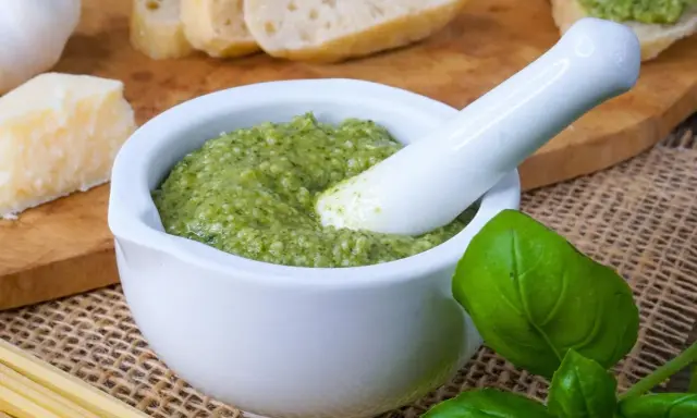 Frisches Pesto im Mörser, bereit für ein köstliches Rezept. Daneben liegen Brot, Parmesan, Knoblauch und Basilikum.