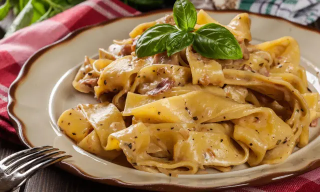 Breite, cremige Pappardelle-Nudeln mit Speck und Kräutern, garniert mit Basilikum.