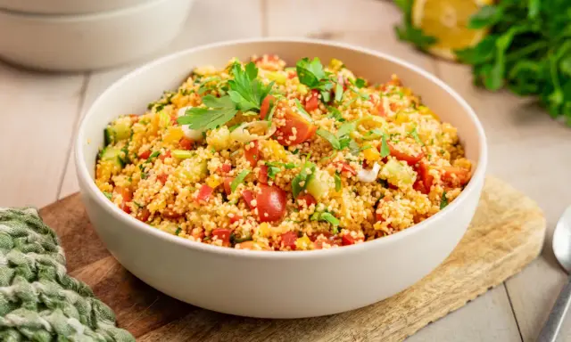 Frischer Couscous Salat mit Tomaten, Gurken und Paprika, garniert mit Petersilie. Ein leichter und gesunder Genuss.