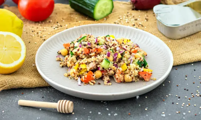 Bunter Quinoa Salat mit Kichererbsen, Tomaten, Gurken und Zwiebeln, garniert mit Zitronenspalten.