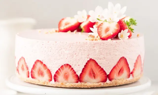 Ein zarter Erdbeer Cheesecake, verziert mit frischen Erdbeerscheiben und Blüten. Dieses Erdbeer Cheesecake Rezept sieht köstlich aus!