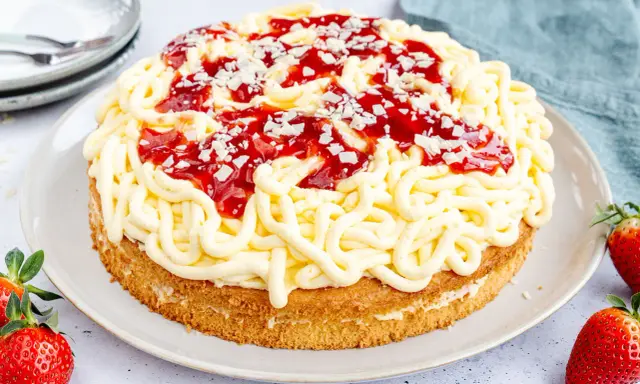 Eine Spaghettieis Torte mit Erdbeersoße und weißen Schokostückchen, die an Spaghetti erinnert.