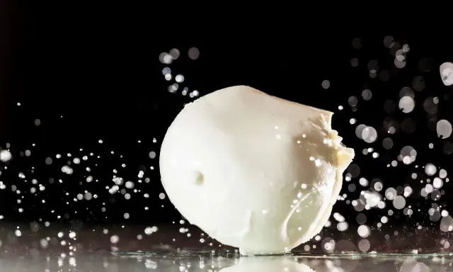 Ein frischer Fior di Latte, der auf einer spiegelnden Oberfläche liegt, umgeben von Wassertropfen und Bokeh-Lichtern.