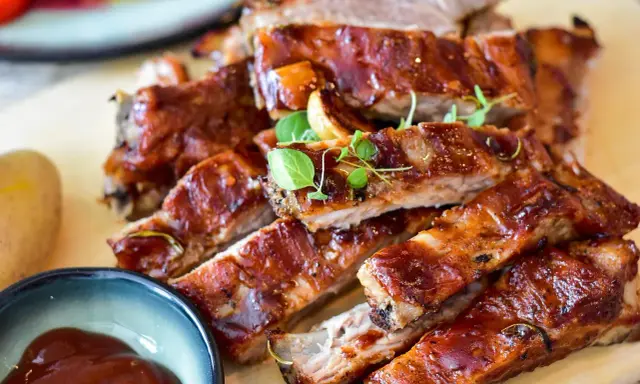 Saftige Spareribs mit glänzender Marinade, garniert mit frischen Kräutern. Dazu eine Schale BBQ-Sauce und eine Kartoffel.