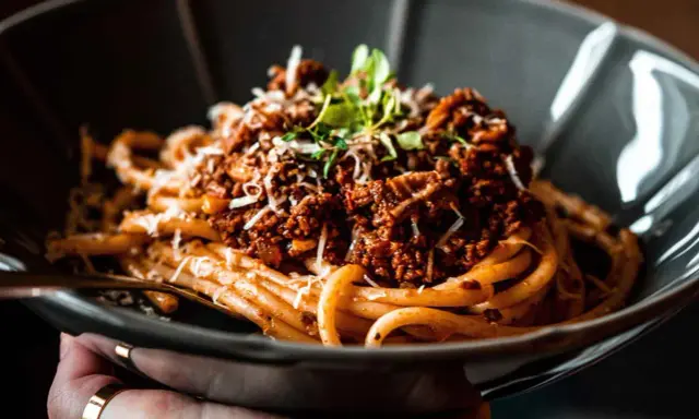 Eine Schüssel mit herzhaftem Pasta al Ragu, garniert mit frischen Kräutern und geriebenem Käse.