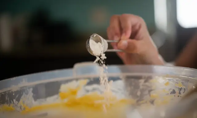 Eine Hand streut Natron aus einem Löffel in eine Schüssel mit Teig. Perfekt für das Backen!