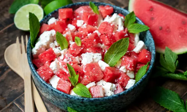 Erfrischender Wassermelonensalat mit Feta und Minze, perfekt für ein leichtes sommersalat rezept. Dazu passen Limettenspalten und Holzbesteck.