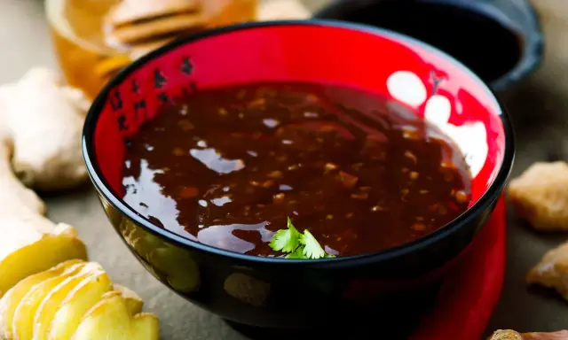 Schwarze Schüssel mit glänzender Teriyaki-Sauce, umgeben von Ingwer, Chili und Honig. Perfekt für dein Teriyaki Sauce Rezept!