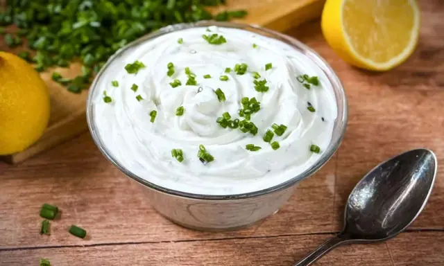 Cremige **sour cream** garniert mit Schnittlauch, daneben Zitronenspalten und ein Löffel.