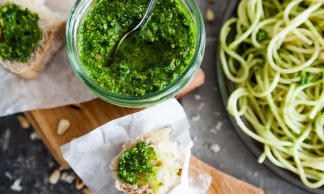 Frisches Basilikumpesto rezept in einem Glas, daneben Brot mit Pesto und eine Portion Spaghetti. Perfekt für ein schnelles Mittagessen.