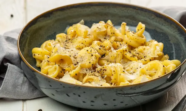 Eine Schüssel mit italienischen Nudeln, bestreut mit Parmesan und schwarzem Pfeffer, serviert auf einem rustikalen Tisch.