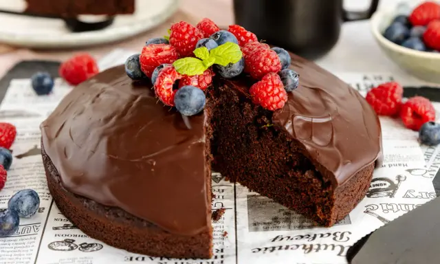 Ein saftiger veganer Schokokuchen mit glänzender Schokoladenglasur, garniert mit frischen Himbeeren und Blaubeeren.