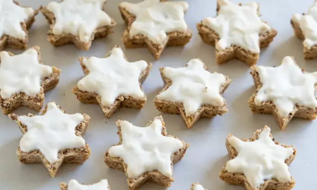 Klassisches zimtsterne rezept: Sterne aus Nüssen, mit weißer Glasur überzogen, bereit zum Genießen.