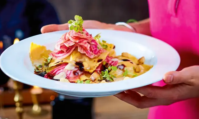Ein Teller mit Ravioli, garniert mit Streifen von roter Bete und Kräutern. Ein Gericht, das perfekt für "Das perfekte Dinner Rezepte" wäre.