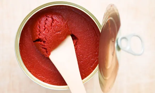 Ein offener Behälter mit leuchtend rotem Tomatenmark, aus dem mit einem Holzspatel eine Portion entnommen wird. Perfekt als Tomatenmark-Ersatz für Saucen und Eintöpfe.