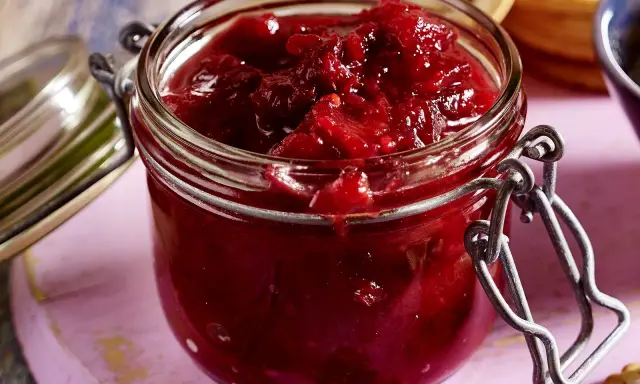 Ein Glas mit leuchtend rotem Zwetschgen-Chutney, bereit, zu Käse oder Gebäck serviert zu werden.