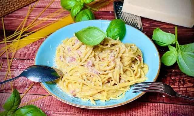 Herzhafte Spaghetti Carbonara mit Speck, garniert mit frischem Basilikum und Parmesan. Ein Klassiker, der immer schmeckt.