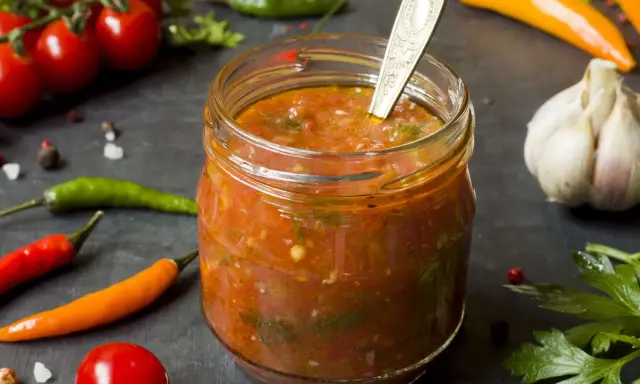 Ein Glas mit würzigem Zucchini-Ketchup, umgeben von frischen Tomaten, Chilis und Knoblauch.