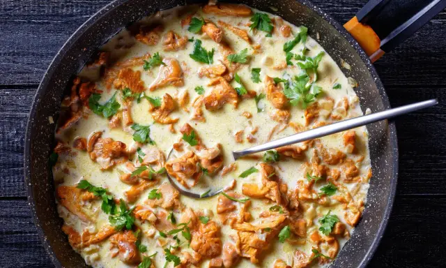 Pfifferlinge in cremiger Rahmsauce, garniert mit Petersilie, in einer Pfanne. Ein Löffel ragt aus der köstlichen Speise.
