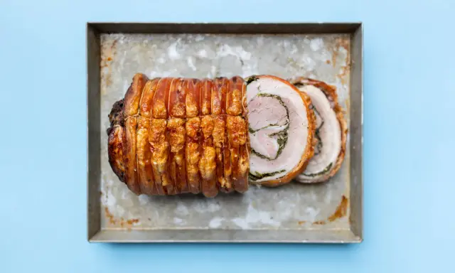 Ein knusprig gebratenes Stück Porchetta, ein italienisches Schweinebraten-Gericht, liegt auf einem Blech.