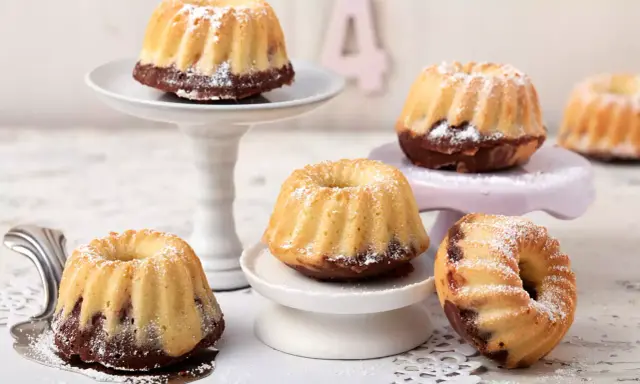 Mehrere kleine, mit Puderzucker bestäubte Mini Gugelhupf-Kuchen mit Schokoladenboden stehen auf verschiedenen Etageren.