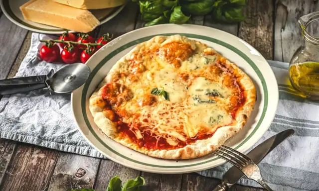 Eine köstliche Pizza Quattro Formaggi mit vier Käsesorten, serviert mit frischen Tomaten und Basilikum auf einem Holztisch.