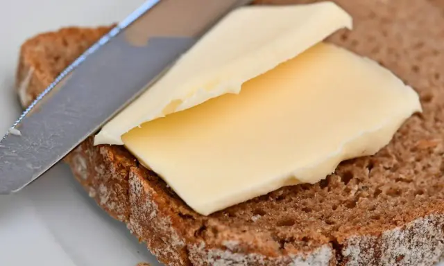 Ein Messer verteilt cremige Butter oder Margarine auf einer Scheibe dunklem Brot.