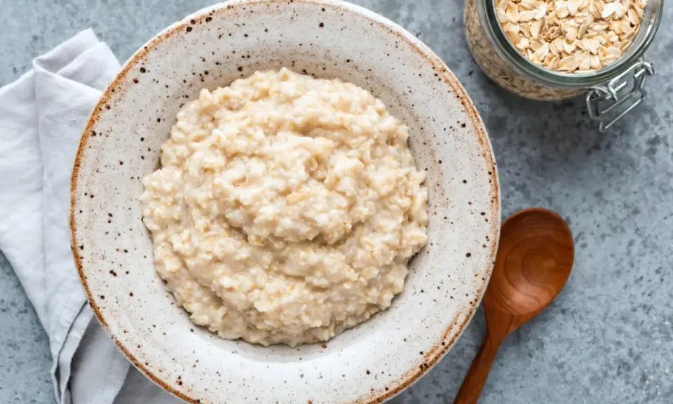 Cremiger Haferbrei im Teller, daneben ein Glas Haferflocken und ein Holzlöffel. Perfekt für ein einfaches Porridge Rezept.