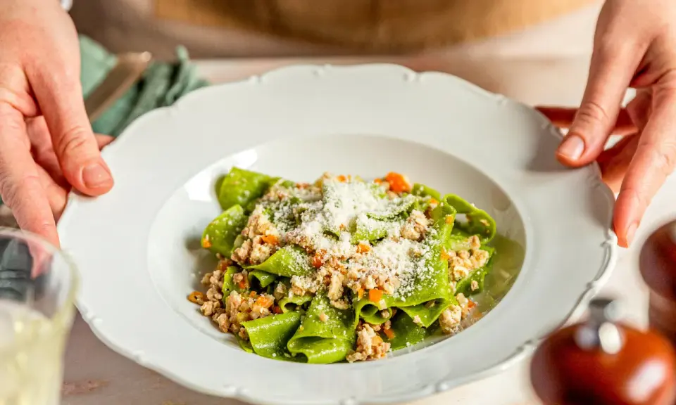 Grüne Bandnudeln mit herzhaftem ragu bianco und Parmesan bestreut, serviert auf einem weißen Teller.